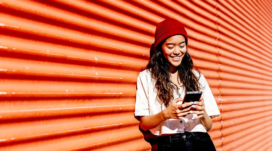 Person using smartphone against red wall outdoors Person using smartphone against red wall outdoors