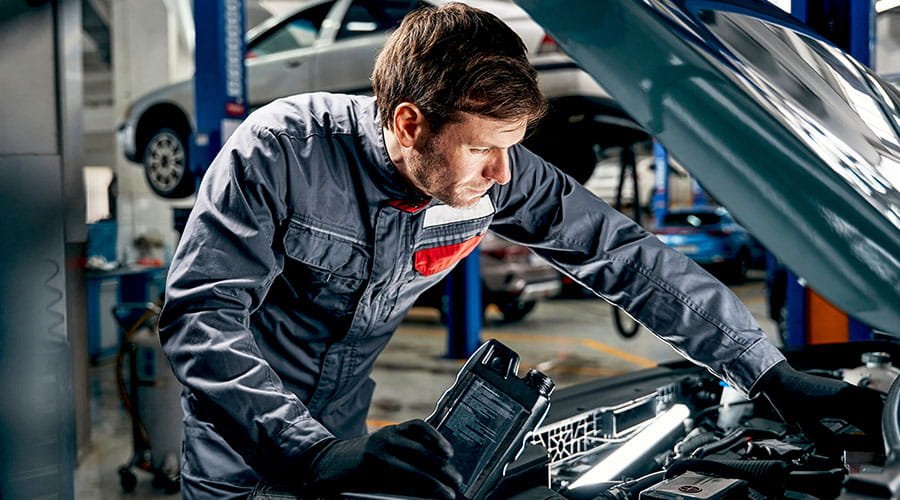 Mechanic working under car hood in automotive workshop Mechanic working under car hood in automotive workshop