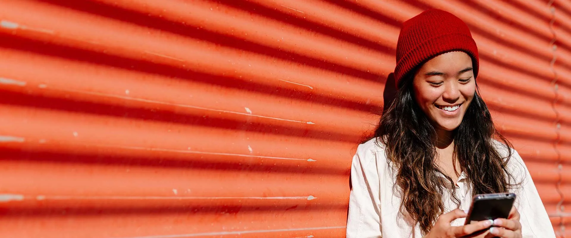 Woman wearing a red beanie using a smartphone against a bright red background Woman wearing a red beanie using a smartphone against a bright red background