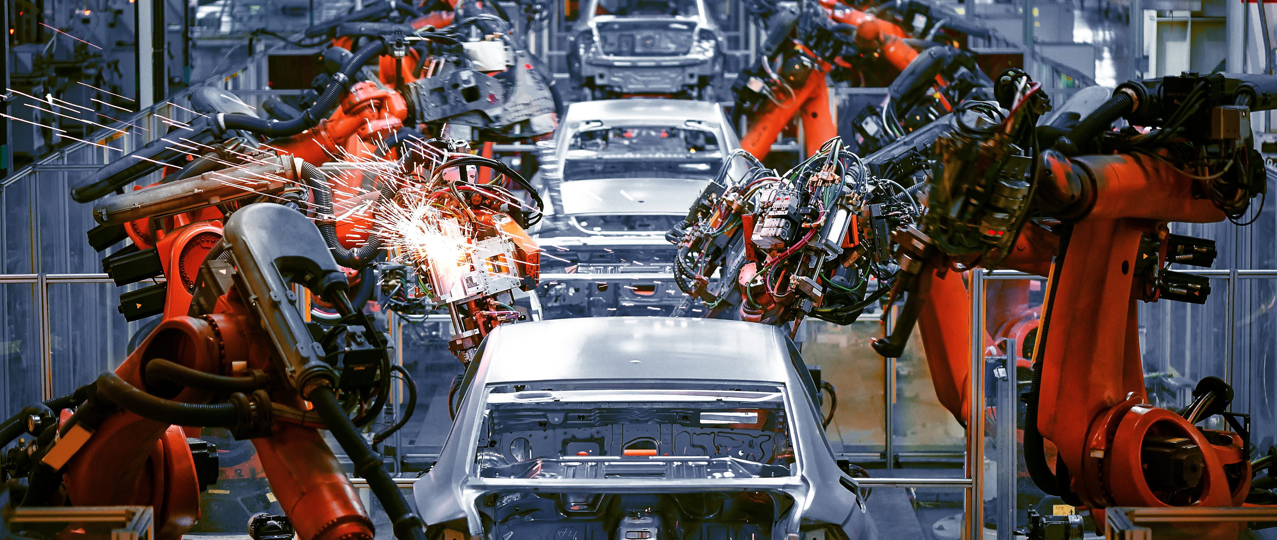 Automated robotic arms assembling cars on a production line in an automotive factory. Sparks fly from welding robots as vehicles move through the assembly process