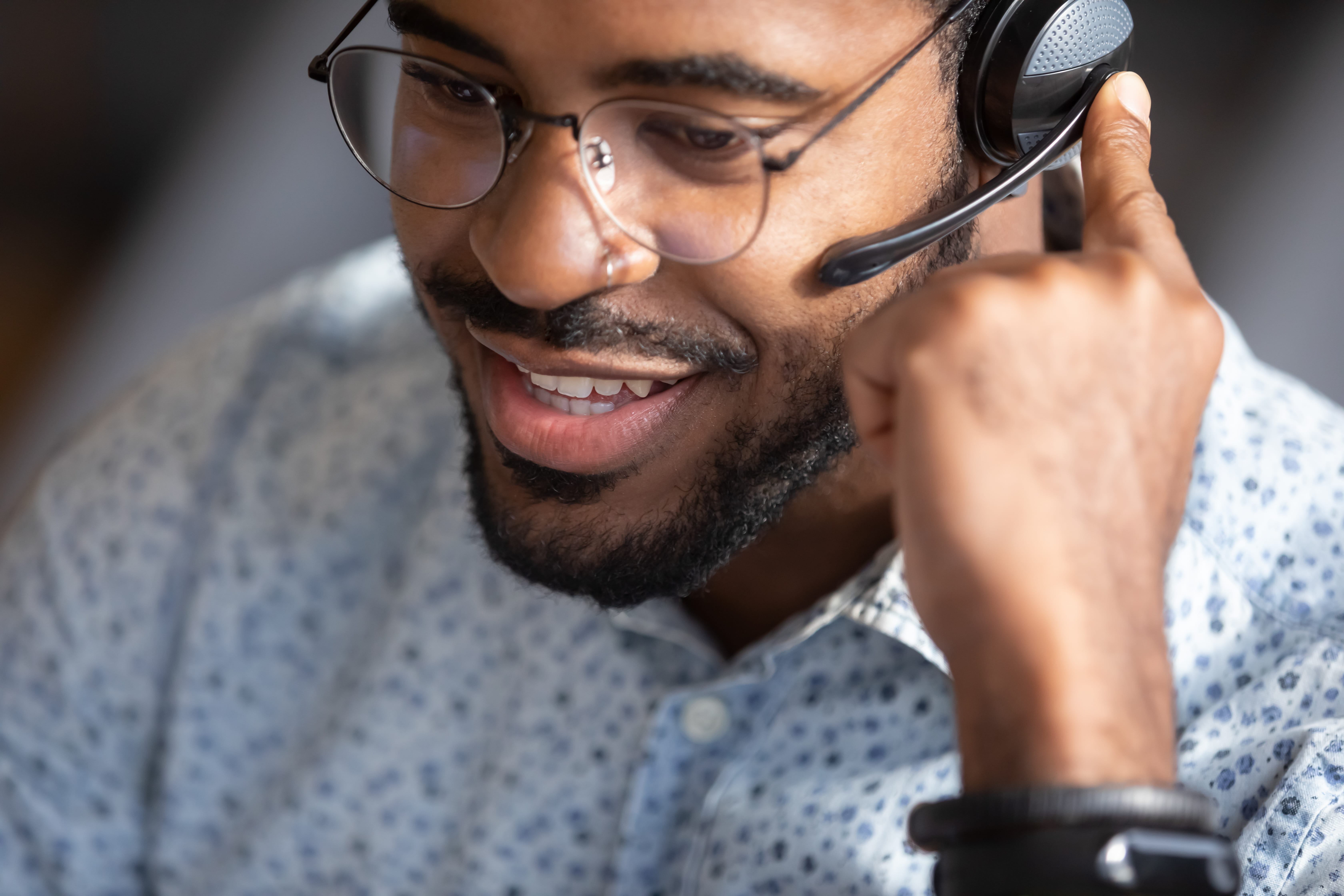 Close-up of a smiling customer service representative wearing glasses and a headset, engaging in a conversation, providing support or assistance
