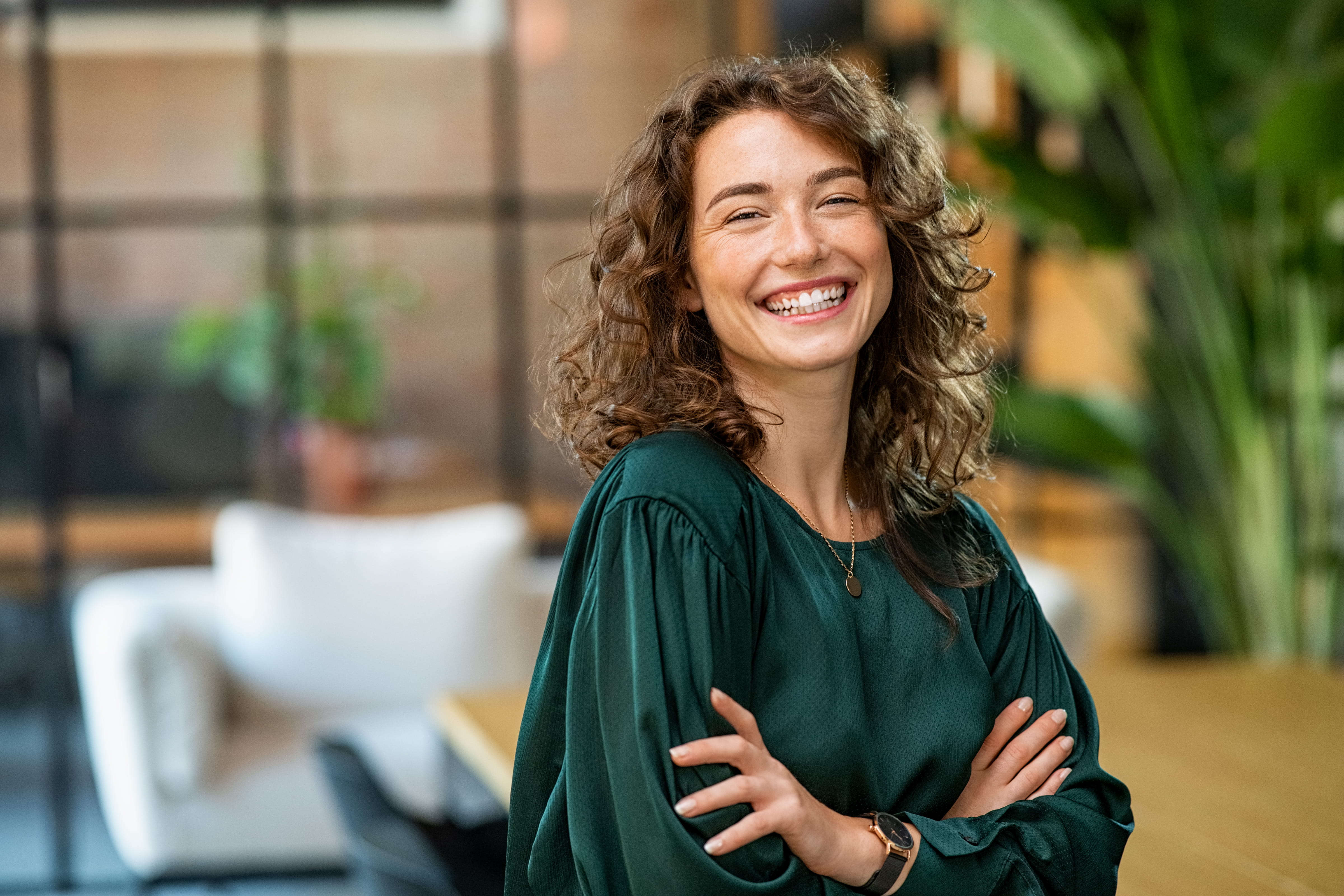 Confident curly haired woman smiling with arm crossed.